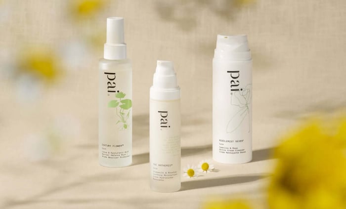 Three Pai skincare products for sensitive skin arranged on neutral background with chamomile flowers