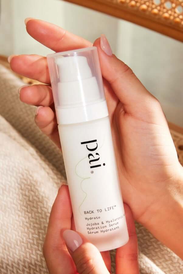 Hands holding Pai Back To Life Hydrating Serum with jojoba and hyaluronic acid in white pump bottle