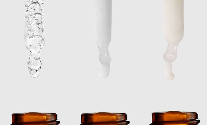 Three amber glass booster bottles with clear serum textures showing water, gel and oil-like consistencies