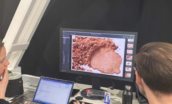 Product development team examining coral-pink mica powder texture on computer screen during British Summer Time formulation process