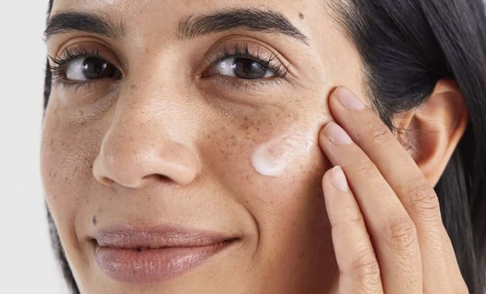 Woman applying white cream to cheek showing natural skin texture with freckles for dark spot treatment
