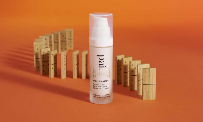 Pai Fade Forward Marine Algae Dark Spot Serum bottle with wooden domino blocks on warm orange background