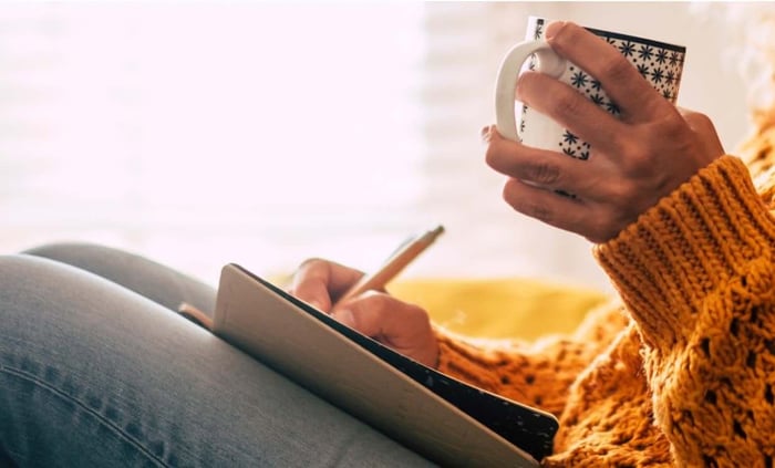 Person in orange sweater holding patterned mug while using tablet to track skincare routine and rosacea triggers