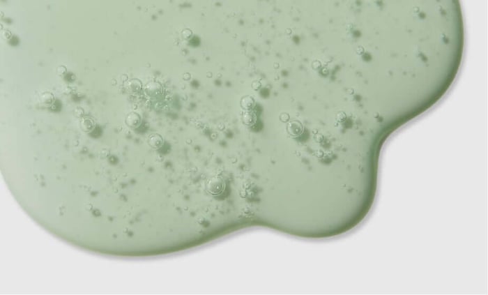 Green foaming face wash with bubbles spreading across white surface, showing gentle cleansing texture