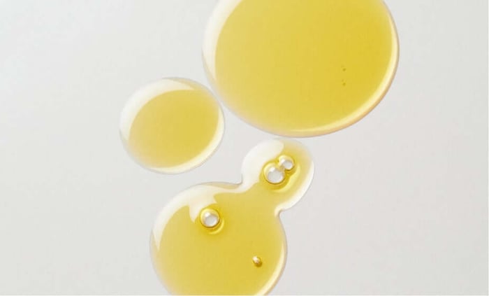 Golden cleansing oil droplets and puddles showing lightweight texture for gentle makeup removal