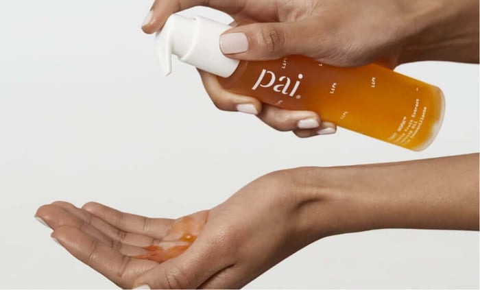 Woman dispensing Pai Light Work Rosehip Cleansing Oil into palm, showing golden cleansing oil texture