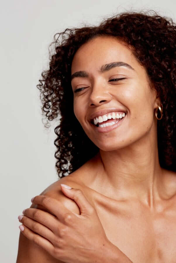 Smiling woman with curly hair and healthy glowing skin showing effective moisture barrier protection