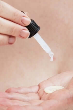 Hand dispensing white serum from dropper bottle onto palm, demonstrating collagen peptide skincare application