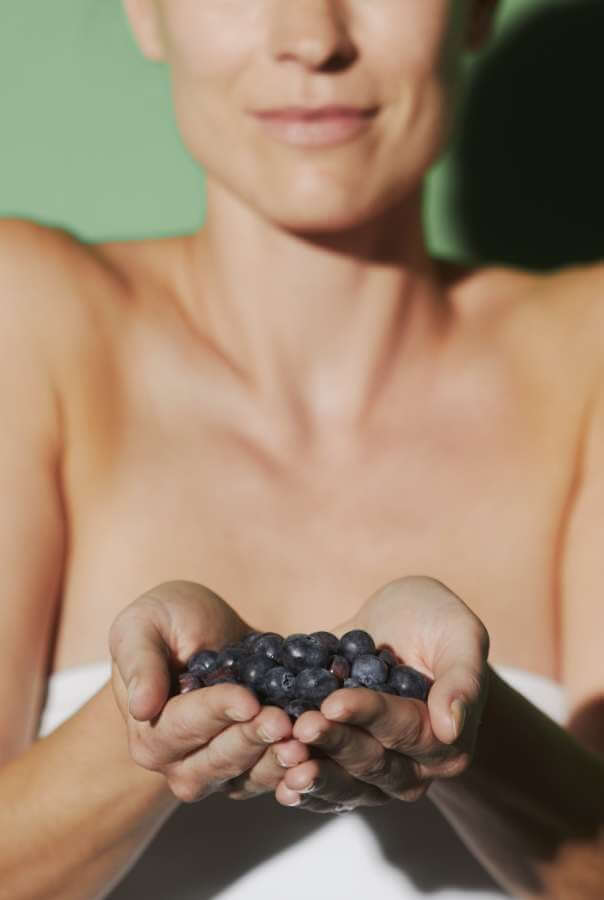 Model with cupped hands holding fresh blueberries against sage green background showcasing antioxidant-rich ingredients for skincare