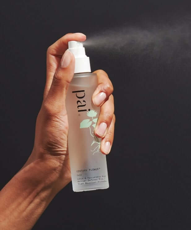 Hands holding Pai Century Flower soothing face mist with pump dispenser against dark background