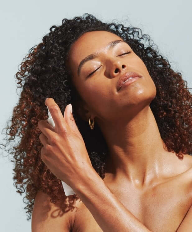 Woman with curly hair enjoying Century Flower face mist with eyes closed, showing peaceful hydration moment