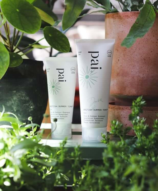Pai British Summer Time sunscreen tubes surrounded by lush green plants in natural sunlight