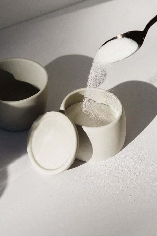 White ceramic bowls and spoon with refined sugar being poured, illustrating dietary factors that can trigger hormonal acne