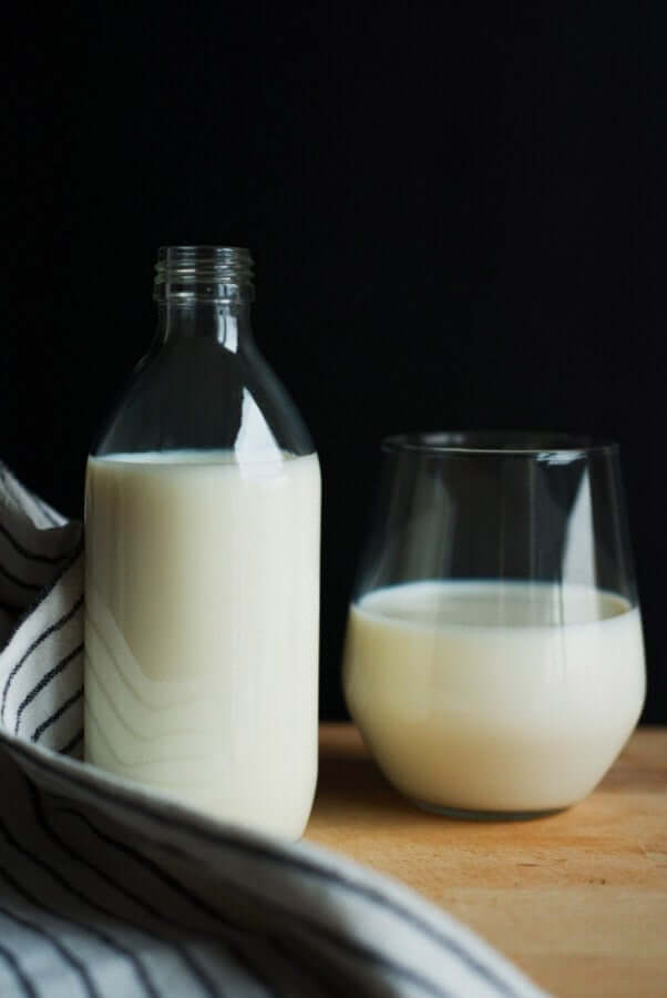 Glass of milk and milk bottle on wooden surface with striped kitchen towel