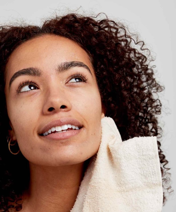 Woman with curly hair gently removing cleanser with soft white cloth, showing gentle skincare routine for hormonal acne