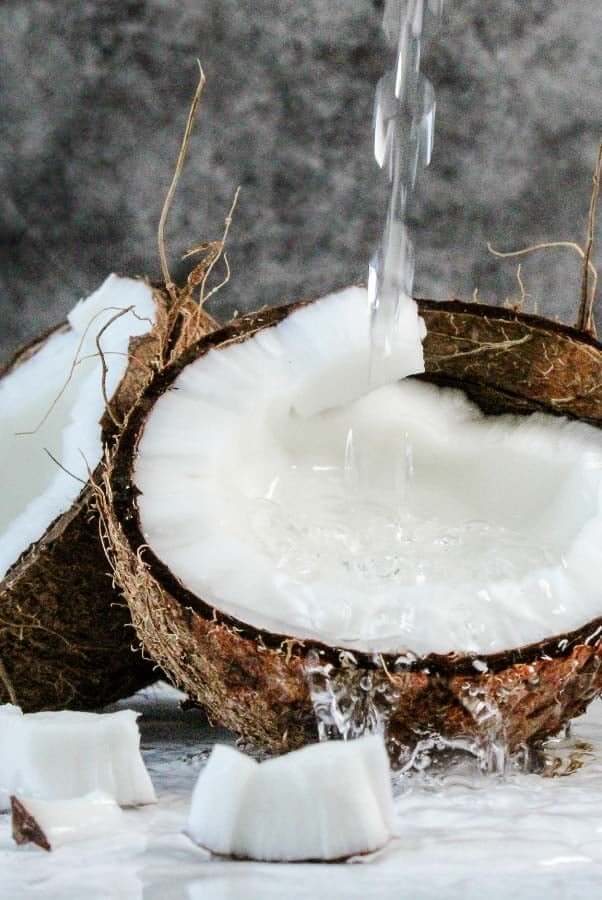 Fresh coconut water pouring into cracked coconut shell showing natural hydration source