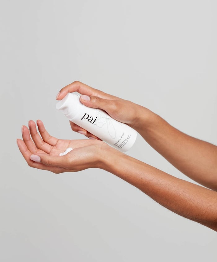 Hands dispensing Pai gentle cream cleanser from white pump bottle for travel skincare routine