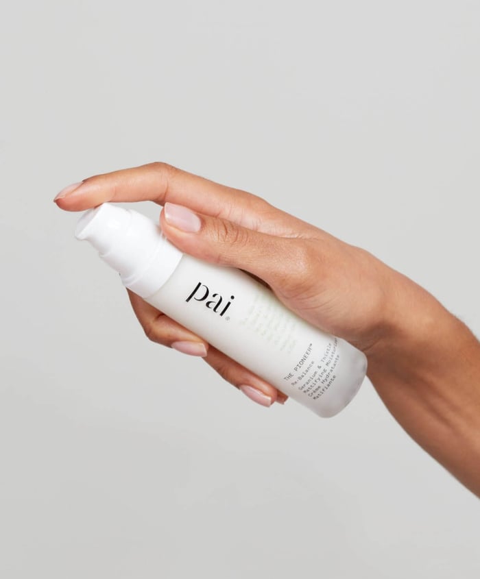 Hand holding Pai The Pioneer Ultra Gentle Face Cream in white pump bottle against neutral background