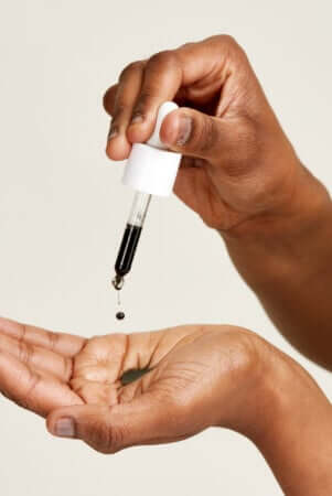 Hands applying face serum drops from white dropper bottle for acne-prone skin