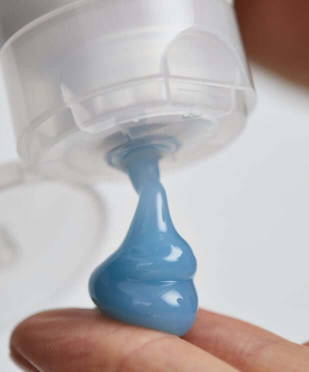 Blue face mask being dispensed from clear pump bottle onto fingertip, showing ocean-blue texture of Resurrection Girl hydrating mask