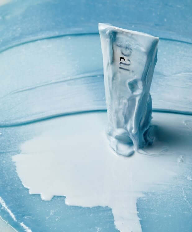 Resurrection Girl hydrating face mask tube standing in puddle of water with ripples on blue surface
