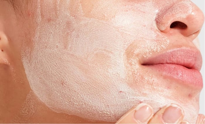 Close-up of person applying white clay mask to face for acne-prone skin treatment