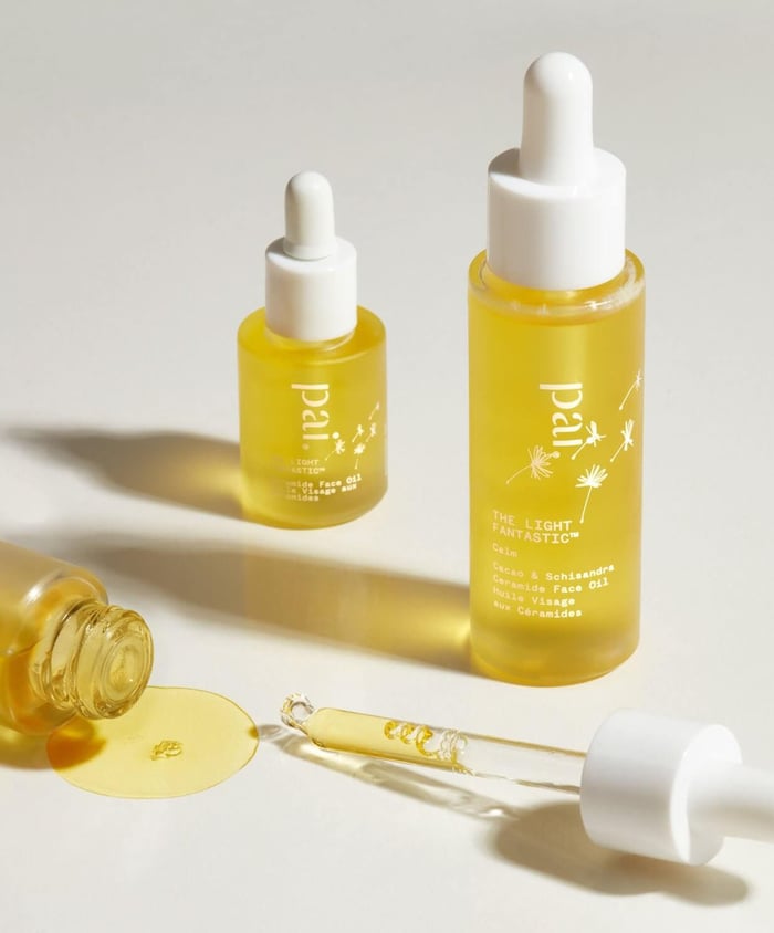 Pai Light Fantastic ceramide face oil bottles with golden oil texture visible in dropper and spilled on white surface