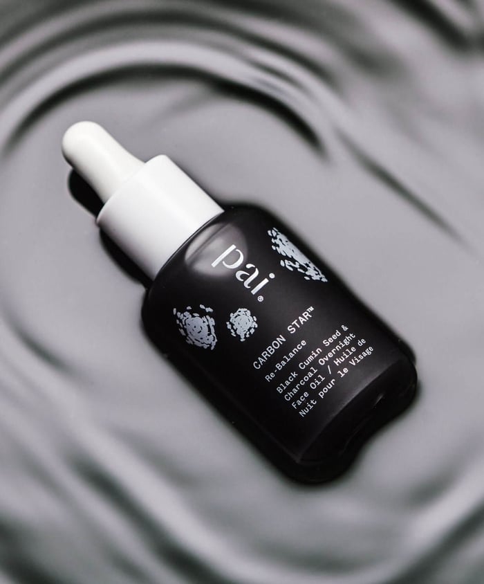 Pai Carbon Star black currant seed face oil with white dropper cap on circular mirror surface