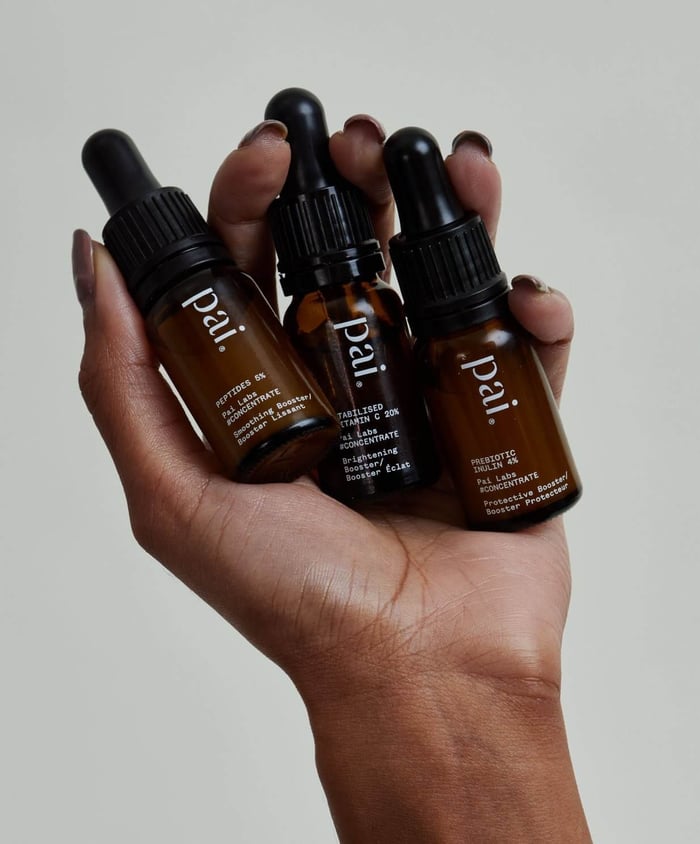 Hand holding three Pai Skincare concentrate serums in amber glass bottles with black droppers