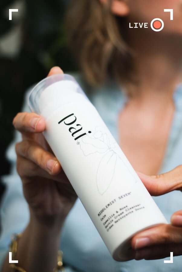 Hands holding Pai Middlemist Seven Camellia & Rose Gentle Cream Cleanser bottle with minimalist white packaging design