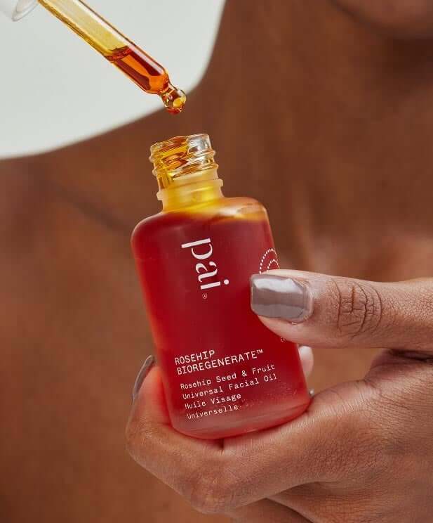 Hands holding Pai Rosehip BioRegenerate Oil bottle with dropper dispensing golden oil drops