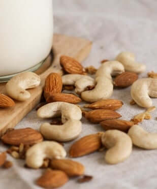 Mixed almonds and cashews scattered on wooden spoon and marble surface, omega-rich nuts for healthy skin