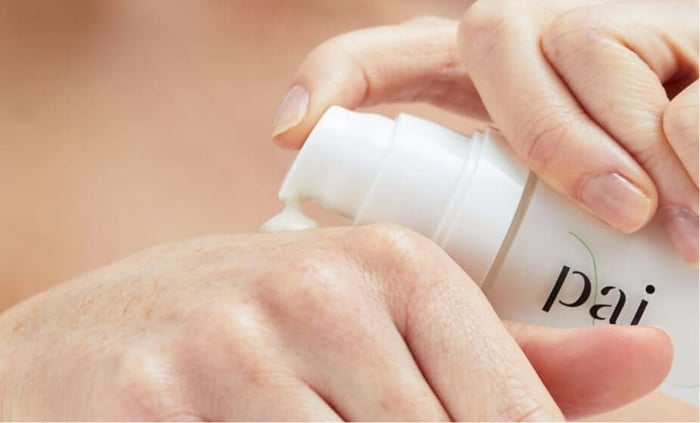 Hands dispensing Pai skincare product from white pump bottle for gentle facial treatment