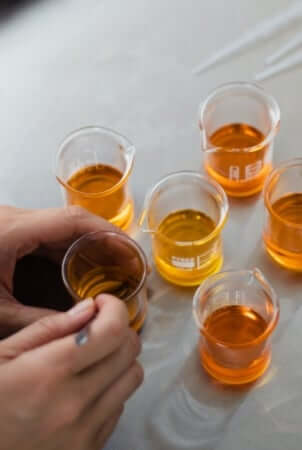 Laboratory beakers containing amber-colored botanical oils and extracts on white surface