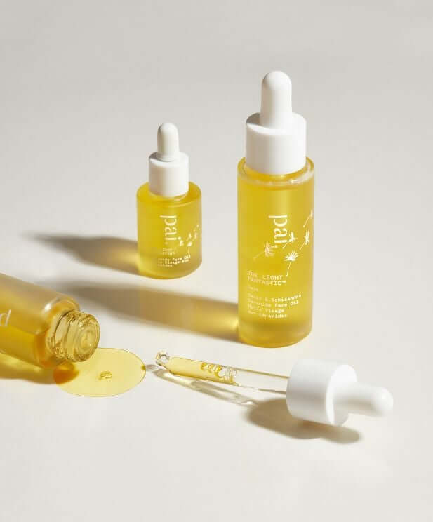 Three golden Pai Rosehip BioRegenerate Oil bottles with white droppers arranged on neutral background, showing face oil texture and natural skincare packaging