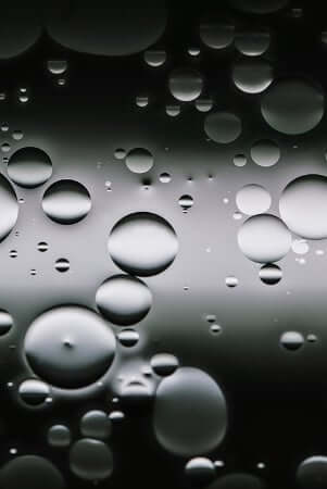Clear water droplets and oil bubbles floating on liquid surface, illustrating the difference between oil and water-based skincare formulations
