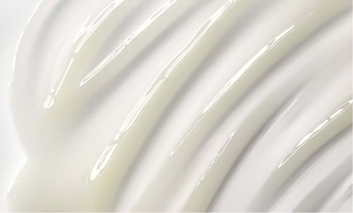 Smooth white moisturizer or serum texture spreading in gentle curves across a clean surface