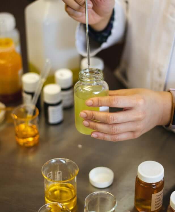 Hands using dropper to blend natural oils in glass bottle during organic skincare formulation process