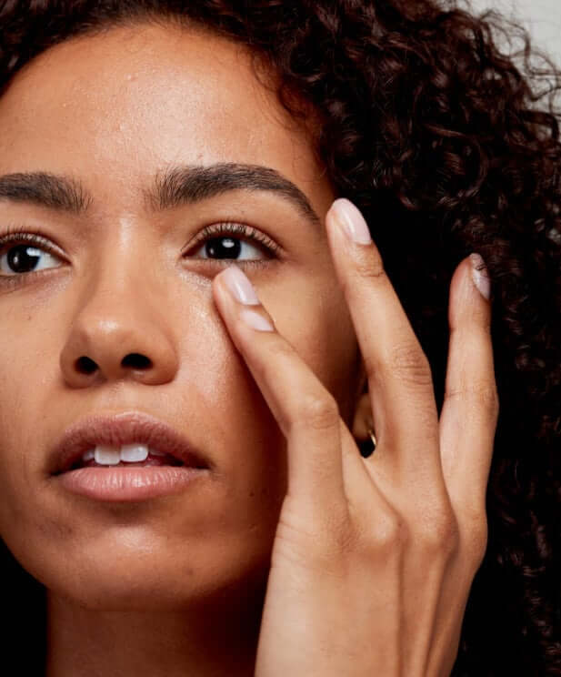 Woman with curly hair gently applying eye cream to under-eye area for sensitive skin care