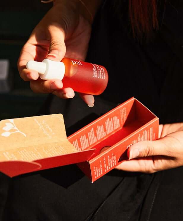 Hands unboxing Pai Rosehip BioRegenerate Oil with red bottle and sustainable packaging