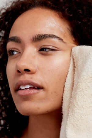 Model with glowing skin holding organic cotton face cloth for sustainable skincare routine