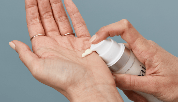 Hands dispensing white moisturiser from pump bottle onto palm, demonstrating proper amount for face application