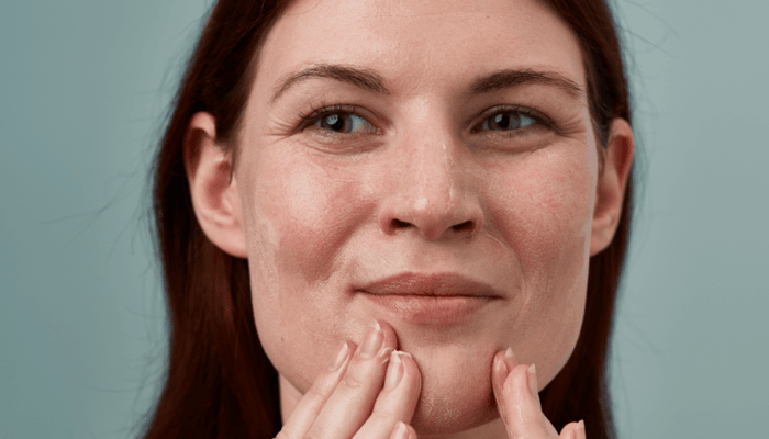 Woman gently touching her chin with fingertips, demonstrating proper facial moisturiser application technique