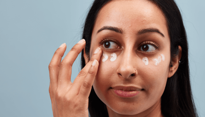 Woman applying small dots of eye cream along orbital bone under eyes demonstrating correct placement technique