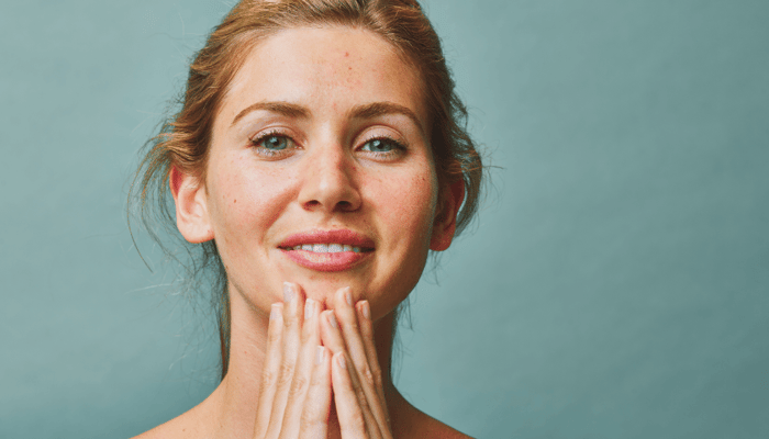 Smiling woman with natural-looking skin cupping hands under her chin against soft green background