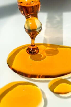 Golden rosehip oil dropping from glass dropper onto white surface, showing the rich amber texture of this nourishing face oil