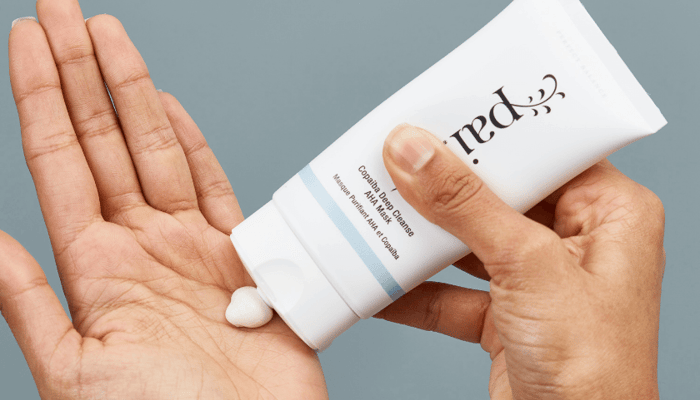 Hands squeezing white Pai skincare cleanser from tube into palm, showing creamy texture
