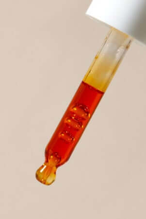Golden rosehip oil droplet falling from glass dropper bottle against neutral background