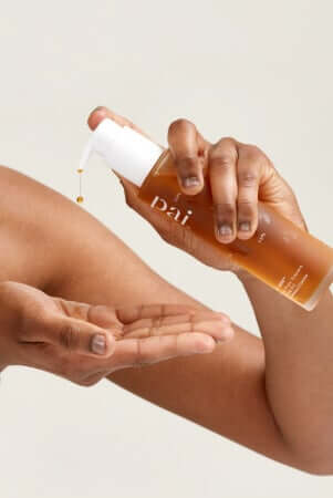 Hands dispensing golden serum from Pai skincare bottle into palm for morning skincare routine