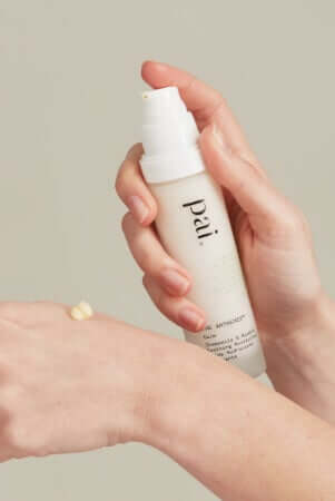 Hands applying Pai skincare serum from white pump bottle, demonstrating morning skincare routine application